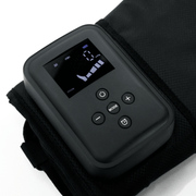 A close-up of the HEALiX Flow by HEALiX Infrared, a black electronic device with a digital display and control buttons, shown on textured black fabric. The screen displays numbers, icons, and settings for time and mode.