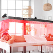 A man enjoys a full-body session under the RLT Home Total Spectrum ELITE Red Light Therapy Panel by RLT Home, while a person in pink uniform stands in the bright, modern room with plants and soft lighting.