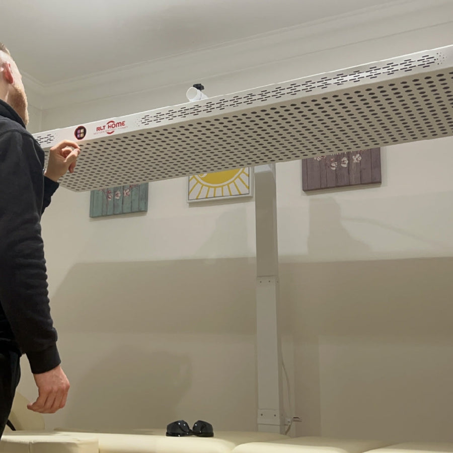 A person stands next to the RLT Home Total Spectrum ELITE Red Light Therapy Panel by RLT Home in a room with light walls and decorative art, showcasing its potential for full-body, professional-grade treatment at home.