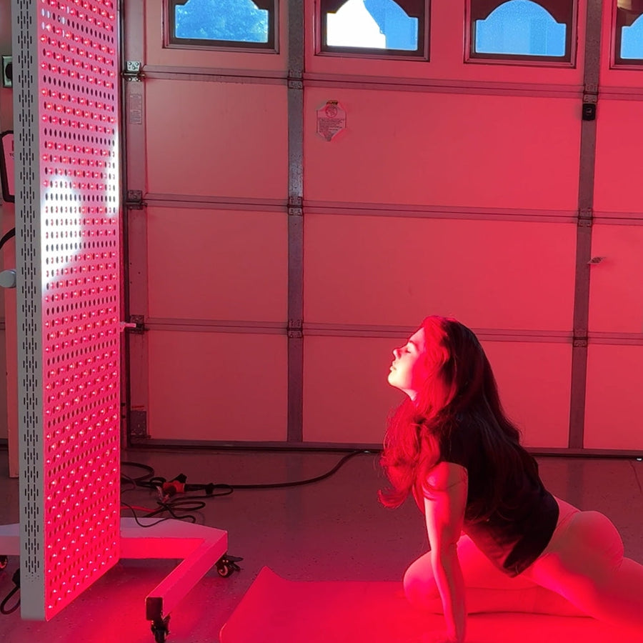 A woman practices yoga in her garage, performing an upward-facing dog pose on a mat while facing the RLT Home Total Spectrum ELITE (7 Wave 864 LEDs) red light therapy device, enjoying mitochondrial activation as part of her wellness routine.