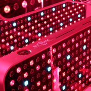 Close-up of the RLT Home Total Spectrum MAX Red Light Therapy Panel by RLT Home, featuring numerous red and a few blue LEDs illuminated and reflected in a mirror—ideal for mitochondrial stimulation and holistic wellness.