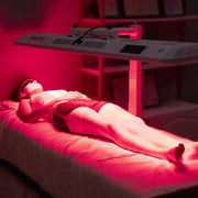 A person relaxes under the RLT Home Total Spectrum ULTRA (7 Wave 480 LEDs) red light therapy device, wearing goggles as a soothing red glow fills the dim room, creating a calming atmosphere that promotes full-body wellness.