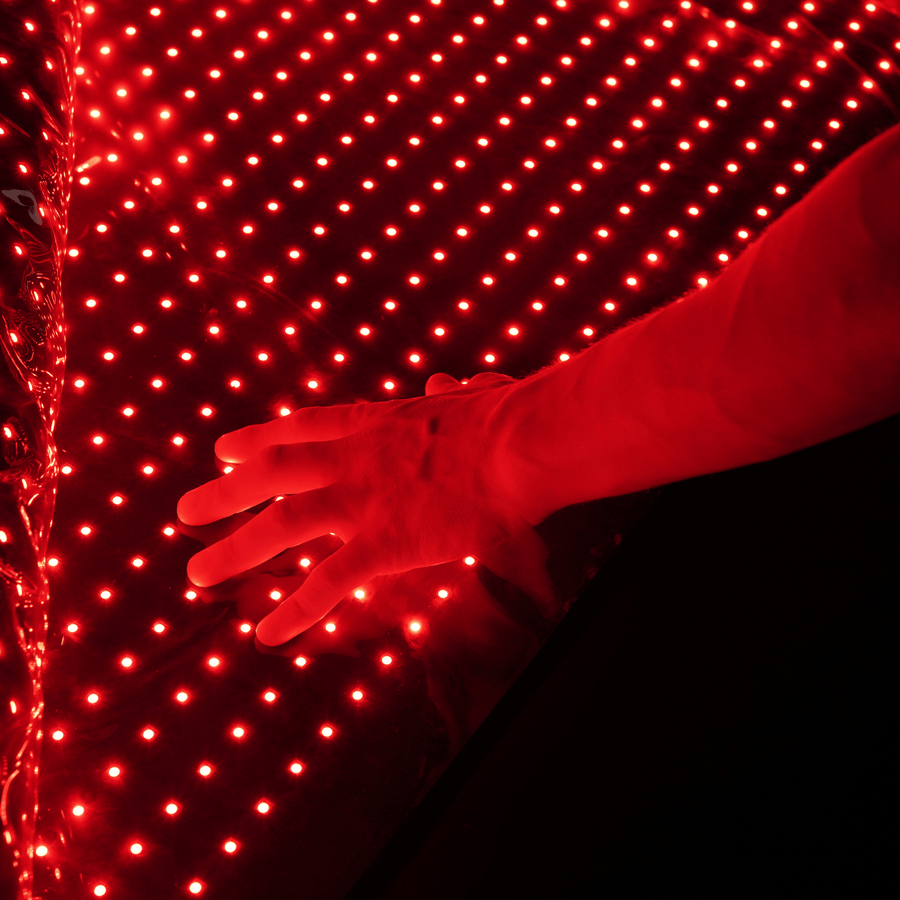 A hand reaches toward the glowing surface of the HEALiX Infrared Elevate Light Pod, its bright red LEDs creating a futuristic effect reminiscent of advanced red light therapy for effective pain relief.