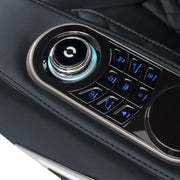 Close-up of a car’s center console with a round control knob and blue-lit buttons for seat adjustments, offering advanced comfort inspired by Osaki’s 4D+3D Bravo Duo Flex massage chair technology on a black leather armrest.