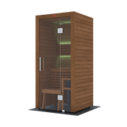 The LuxeWell Life Harvia Utu, a heat-treated 1-person indoor sauna, features Nordic spruce with horizontal slats, a glass door, wooden bench, and soft green LED lighting on the back wall. It stands on a dark mat against a plain white background.