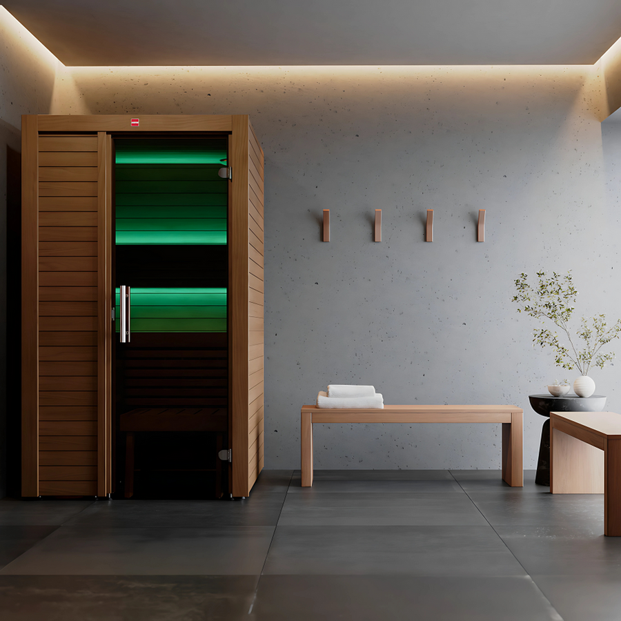 A modern, minimalist spa room features the LuxeWell Life Harvia Utu heat-treated 1-person indoor sauna, a bench with folded towels, wall hooks, a small table, and a potted plant against concrete and tile. Soft lighting enhances the calm ambiance.