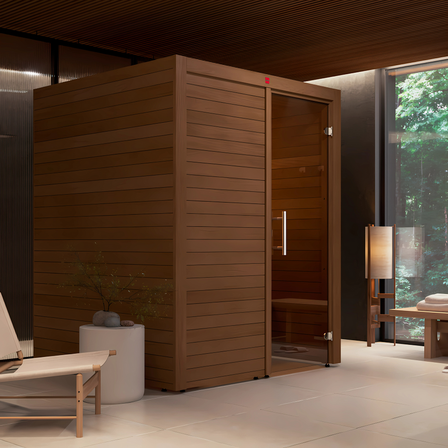 A LuxeWell Life Harvia Utu heat-treated 1-person indoor sauna is set in a minimalist, well-lit room with light floors, a lounge chair, a small table, and a large window overlooking lush green trees.