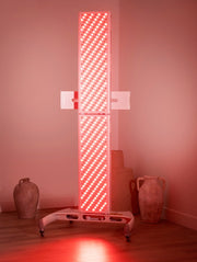 The MitoPRO+ | Red Light Therapy Panel Series v2 from Mito Red Light, featuring quad wavelength LEDs for red & near infrared therapy, stands on a wheeled base in a softly lit room with ceramic vases and jars on the wooden floor.