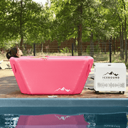 A person relaxes in an Icebound Essentials Pink Endurance Plunge + Chiller by the pool, with trees and a wooden fence in the background.
