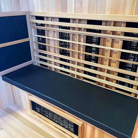 The Finnmark Sauna Cushion for FD-3, made from marine-grade vinyl, adds comfort and style to a modern wooden sauna interior with black bench seating—perfect for relaxing infrared therapy sessions.