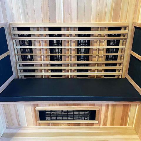 A wooden infrared sauna interior featuring the Finnmark Sauna Cushion for FD-3 in marine-grade vinyl, vertical heaters behind wooden slats, and an extra heater under the bench for enhanced infrared therapy.