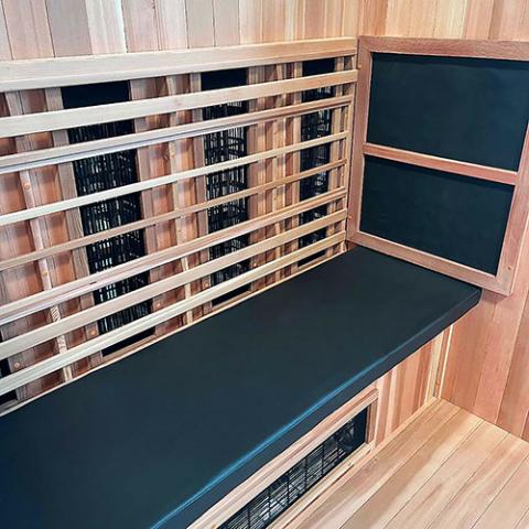 A modern sauna interior features the Finnmark Sauna Cushion for FD-3 in marine grade vinyl on the bench with black infrared heating panels, all set against light wood walls and floors for a sleek, inviting look.