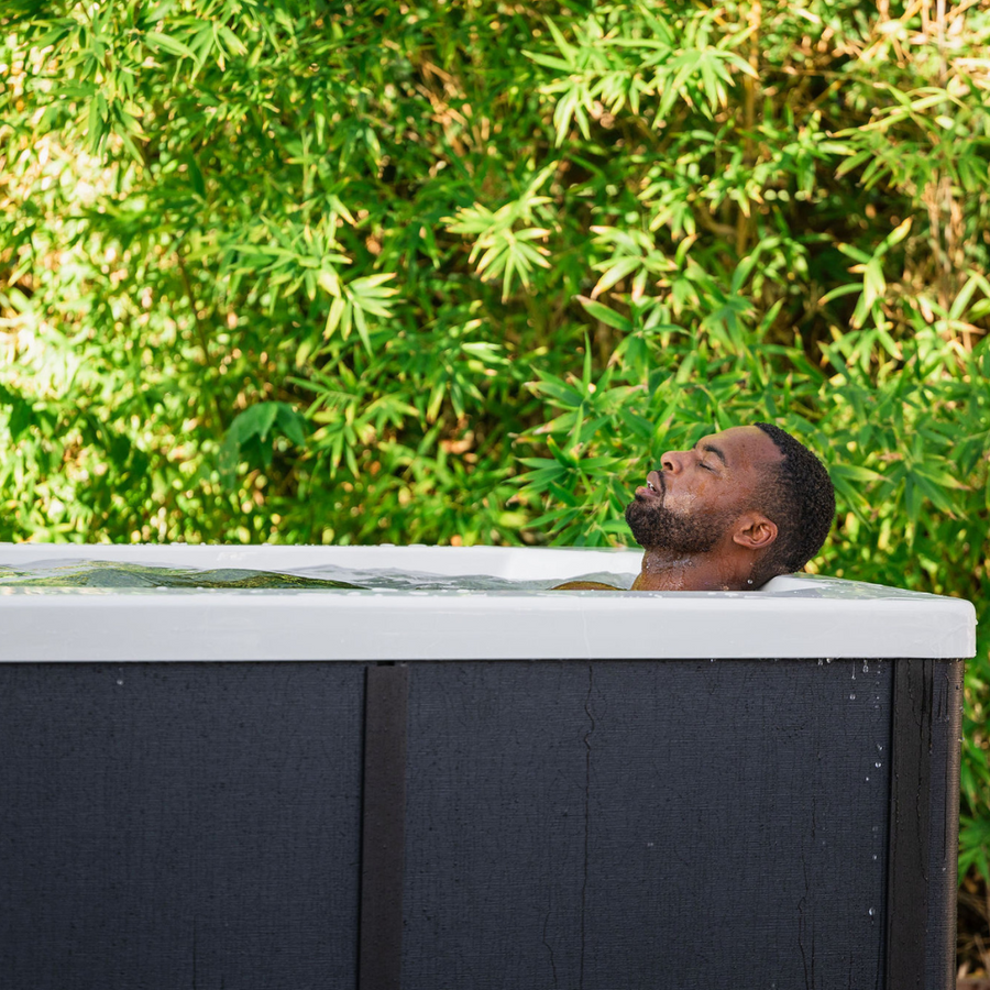 A man relaxes with his eyes closed in The Resolute Pro by Icebound Essentials, enjoying professional-grade recovery outdoors among lush bamboo, with advanced Ozone sanitization under bright natural light.